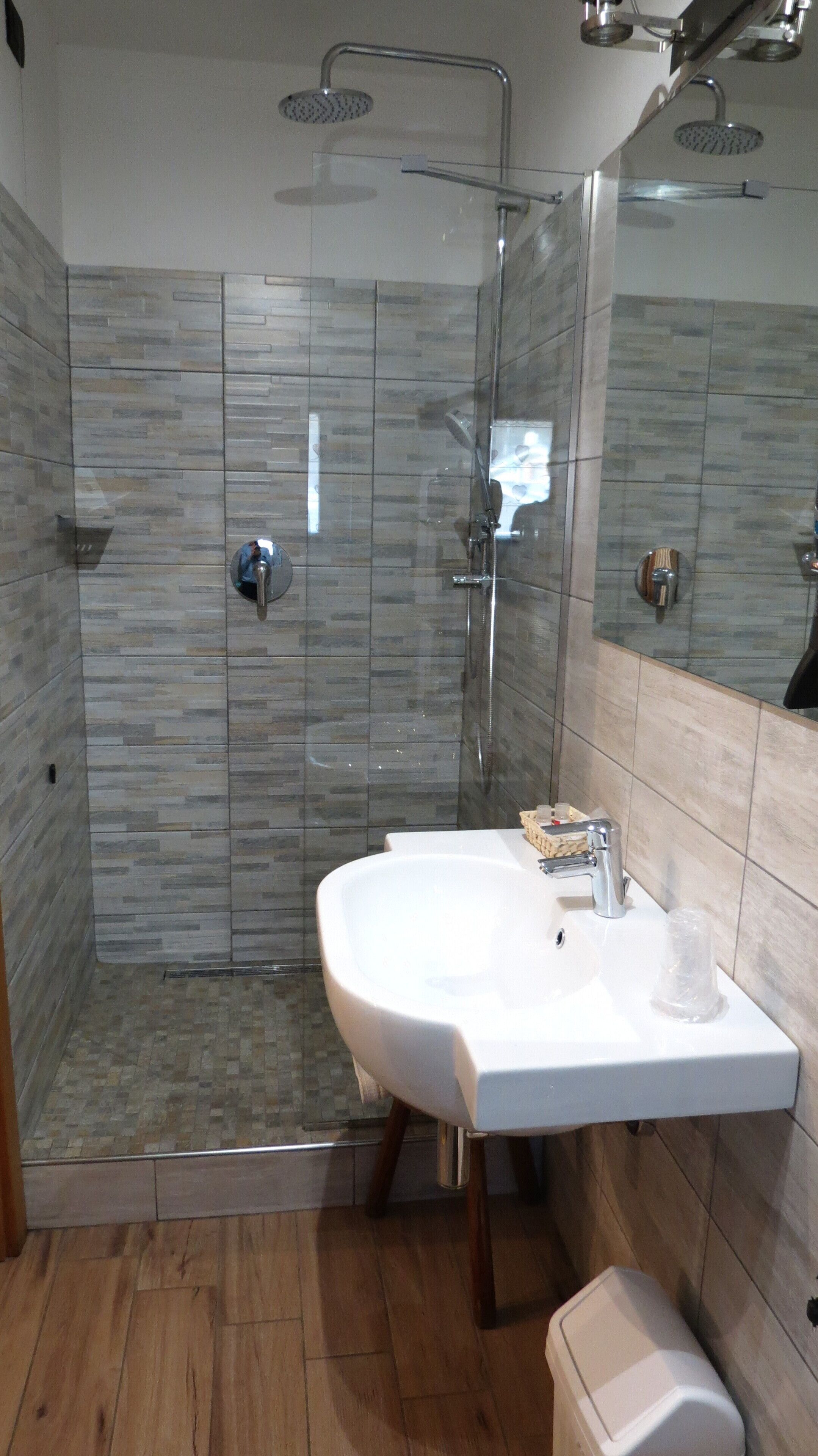 Un baño moderno con ducha de vidrio, lavamanos blanco y piso de madera.