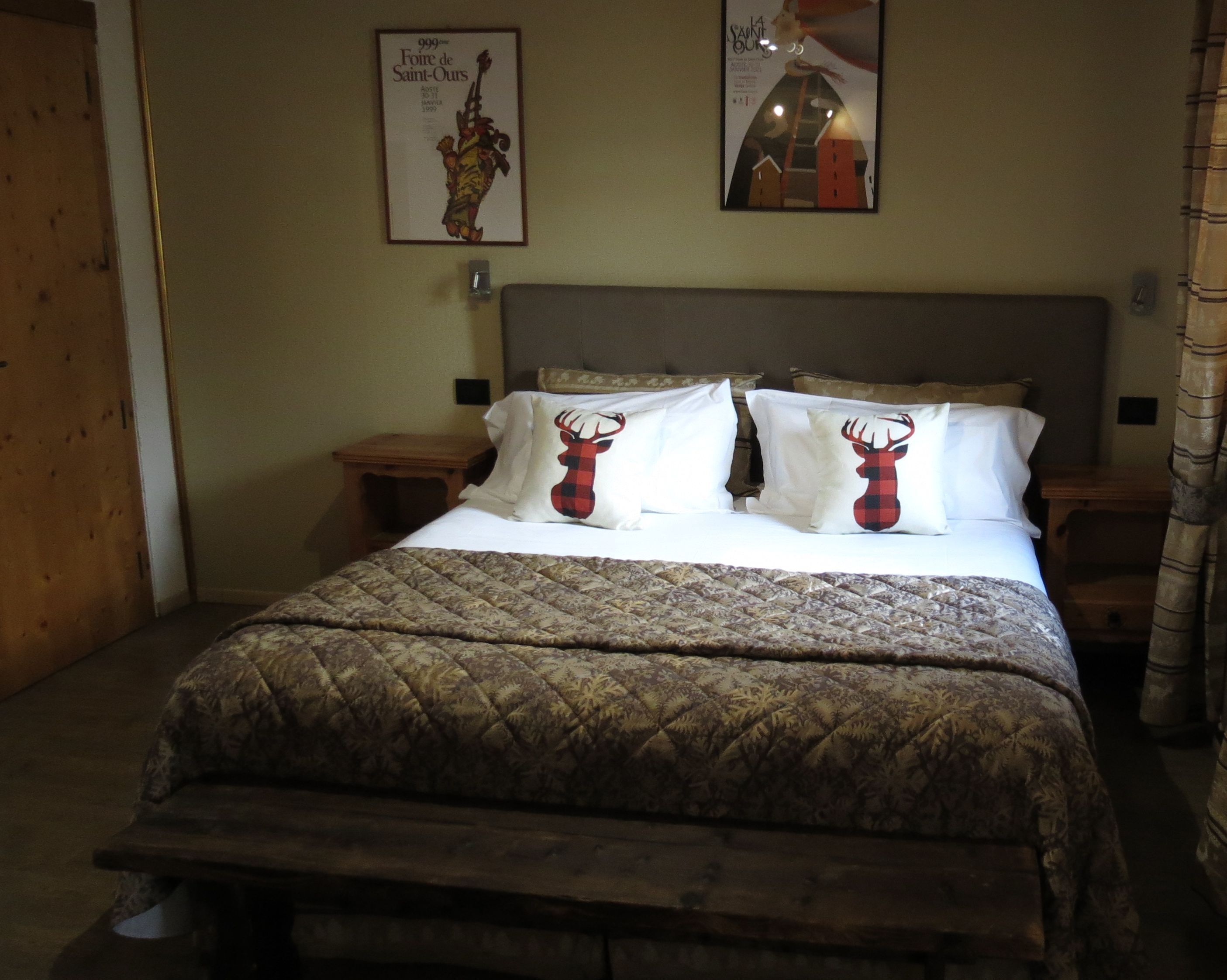 A bed with a patterned quilt, two pillows with deer designs, a framed poster on the wall, and a wooden headboard.