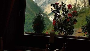 A dining table with a red tablecloth, a vase with red flowers, and a mountain view through a window. - Hotel Astoria (Courmayeur)