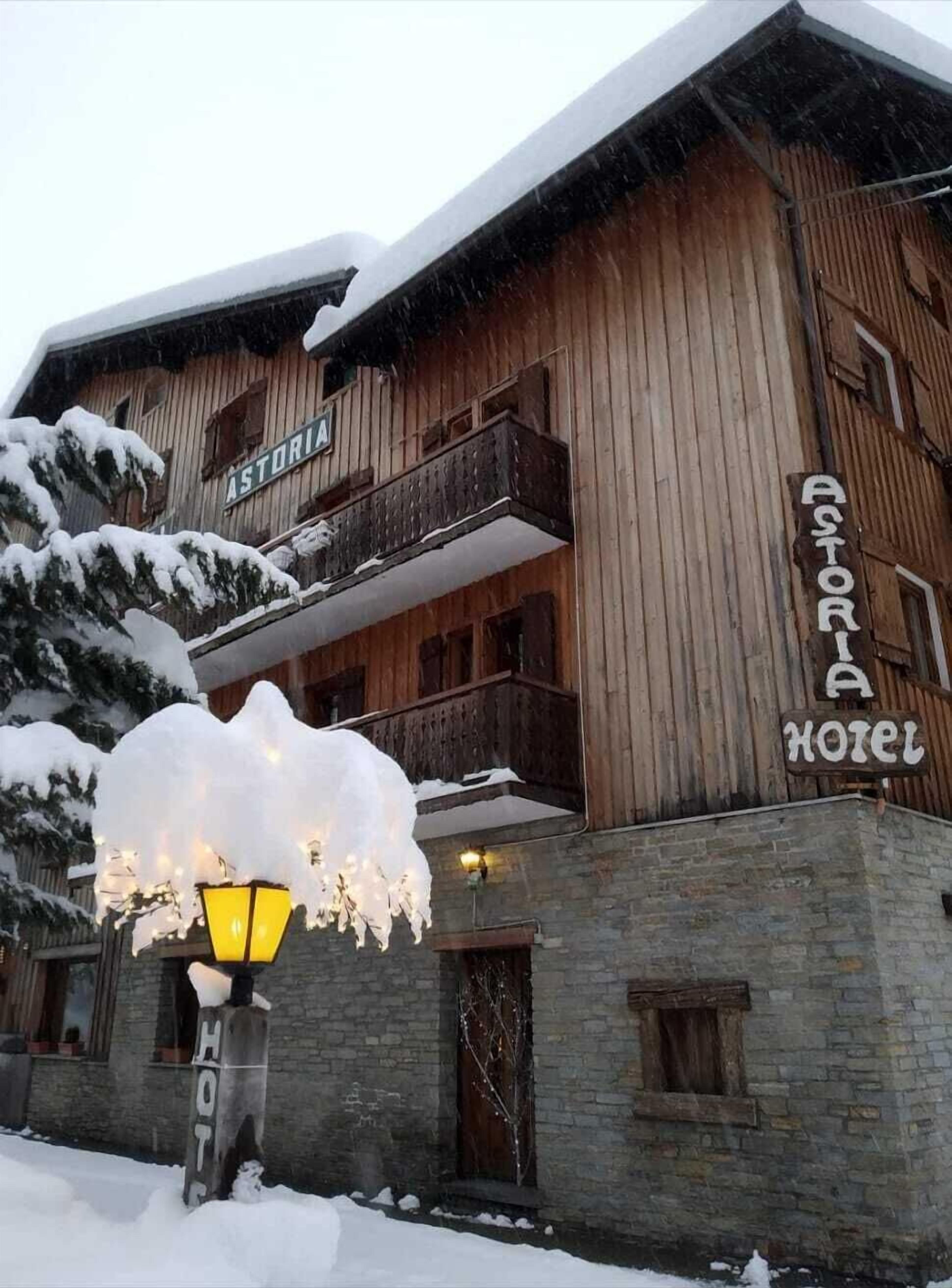 Un edificio de madera con un letrero que dice "ASTORIA HOTEL" y un balcón cubierto de nieve.