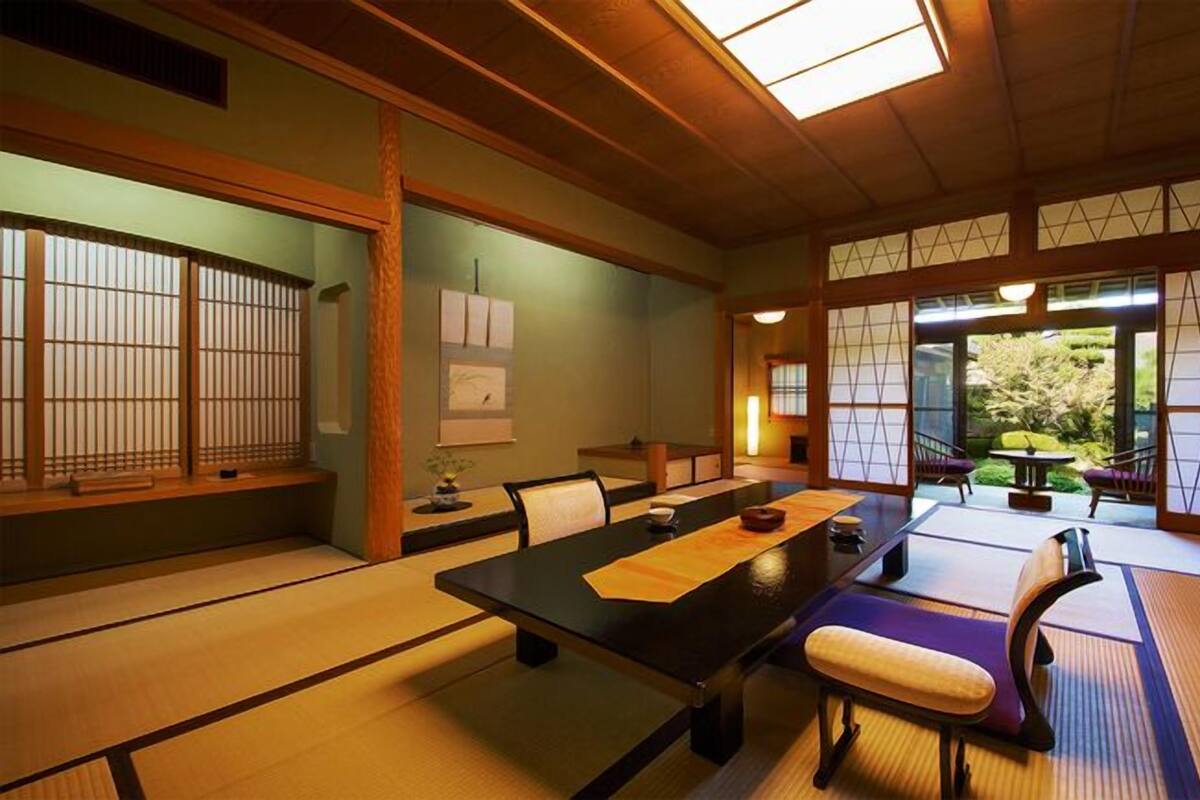 Une pièce de style japonais traditionnel, avec un sol recouvert de tatamis, une table basse, des chaises et des portes coulissantes.