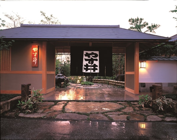 Un edificio japonés tradicional con techo de tejas, una puerta de madera y un camino de piedra que lleva a la entrada.