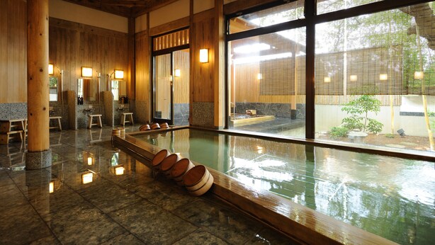 Un onsen japonés tradicional con interiores de madera, suelo de piedra y vistas al jardín circundante.
