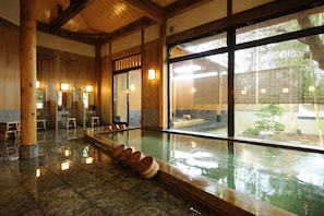A traditional Japanese onsen with a wooden interior, stone flooring, and a view of the surrounding garden. - Ryoutei Ryokan YASUI (Hikone)