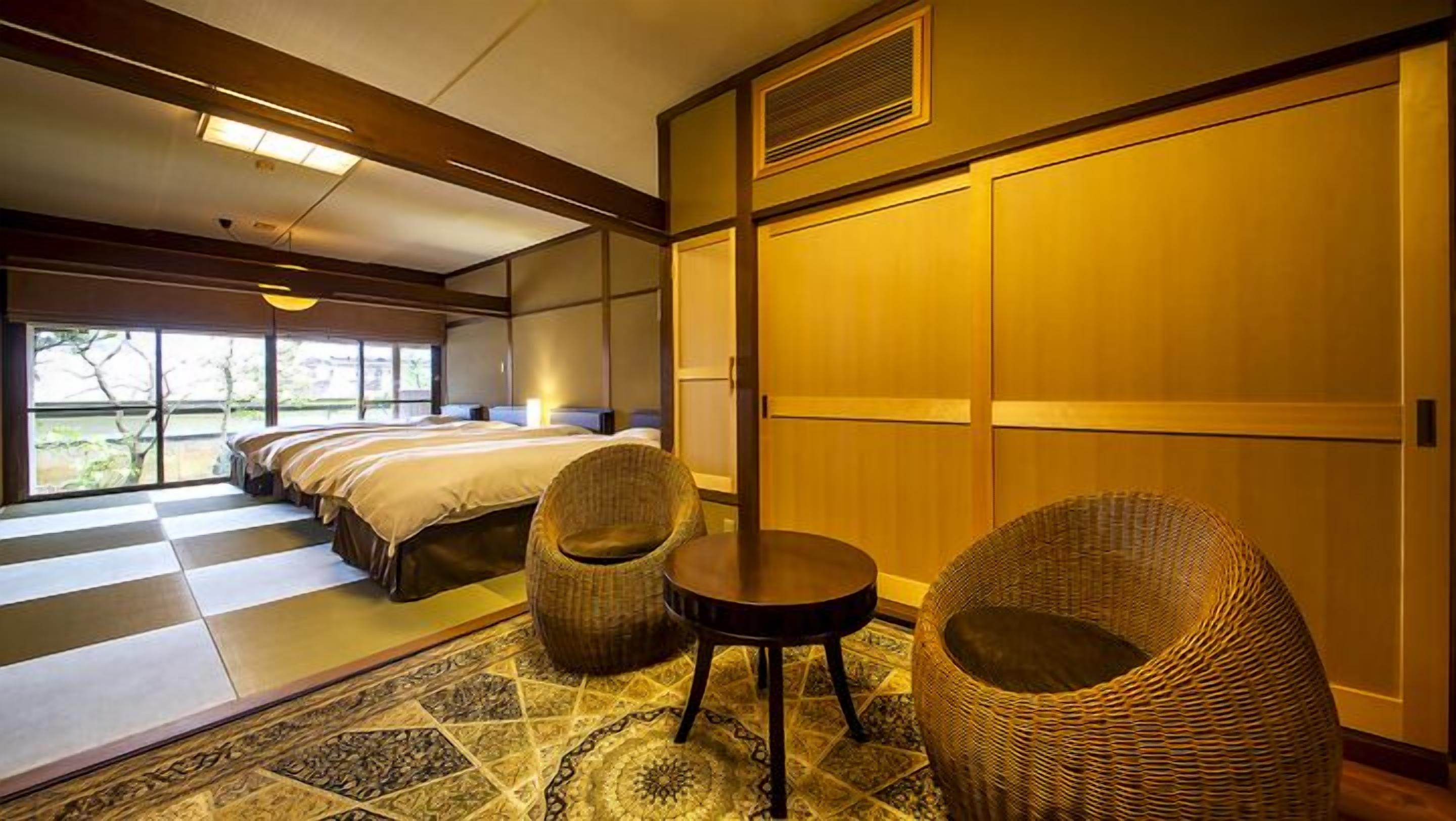 A hotel room with a large bed, a sitting chair, a small table, and a view of the outdoors.
