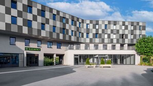 Un hôtel moderne à la façade à motifs géométriques, doté d’une entrée couverte et d’une cour spacieuse agrémentée de jardinières.