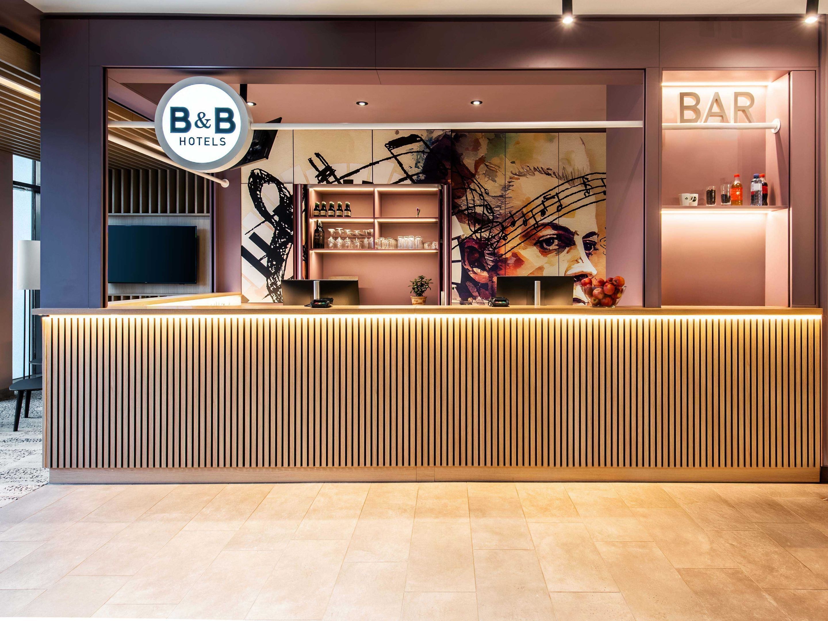 A reception area with a modern design, including a reception desk, a large wall art piece, and a bar area.