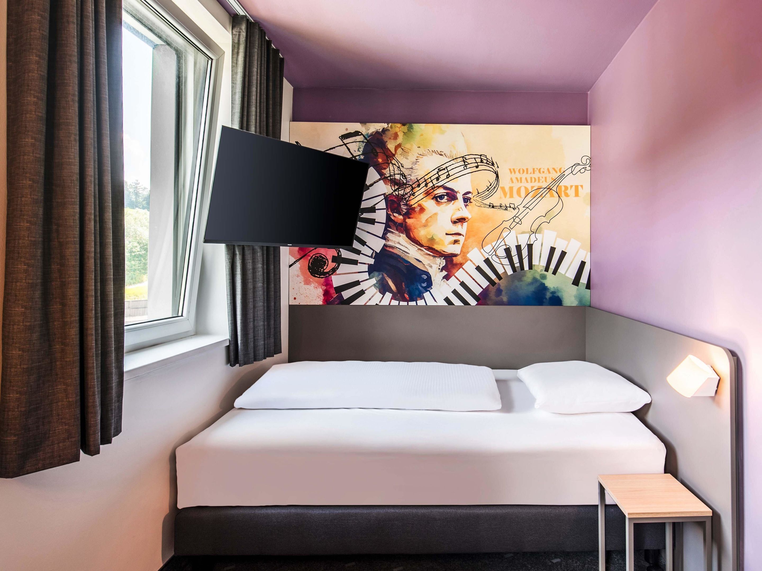 Un dormitorio con cama, televisor montado en la pared y ventana con cortinas.
