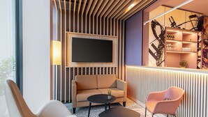 Un salon moderne comprenant un canapé, deux fauteuils, une table basse et un téléviseur à écran plat fixé sur un mur recouvert de panneaux en bois.