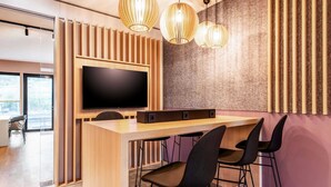 Une cuisine moderne avec un bar en bois, des tabourets de bar noirs, un grand téléviseur à écran plat et des luminaires suspendus.
