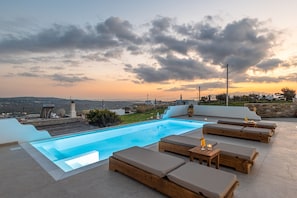 An infinity pool with lounge chairs and tables, set against a sunset sky. - Villa of Roses - Private villa with pool (Naxos)