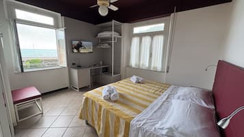 Un dormitorio con cama, escritorio, silla, banco, ventilador de techo y vista al mar.