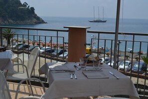 Tavola imbandita per la cena con vista sul mare e un veliero in lontananza.