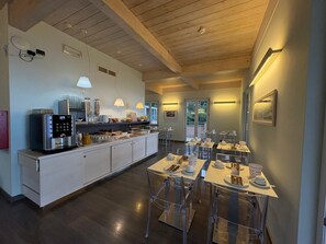 A modern kitchen with a central island, clear dining tables, and a view of the outdoors. - Hotel delle Rose (Bonassola)