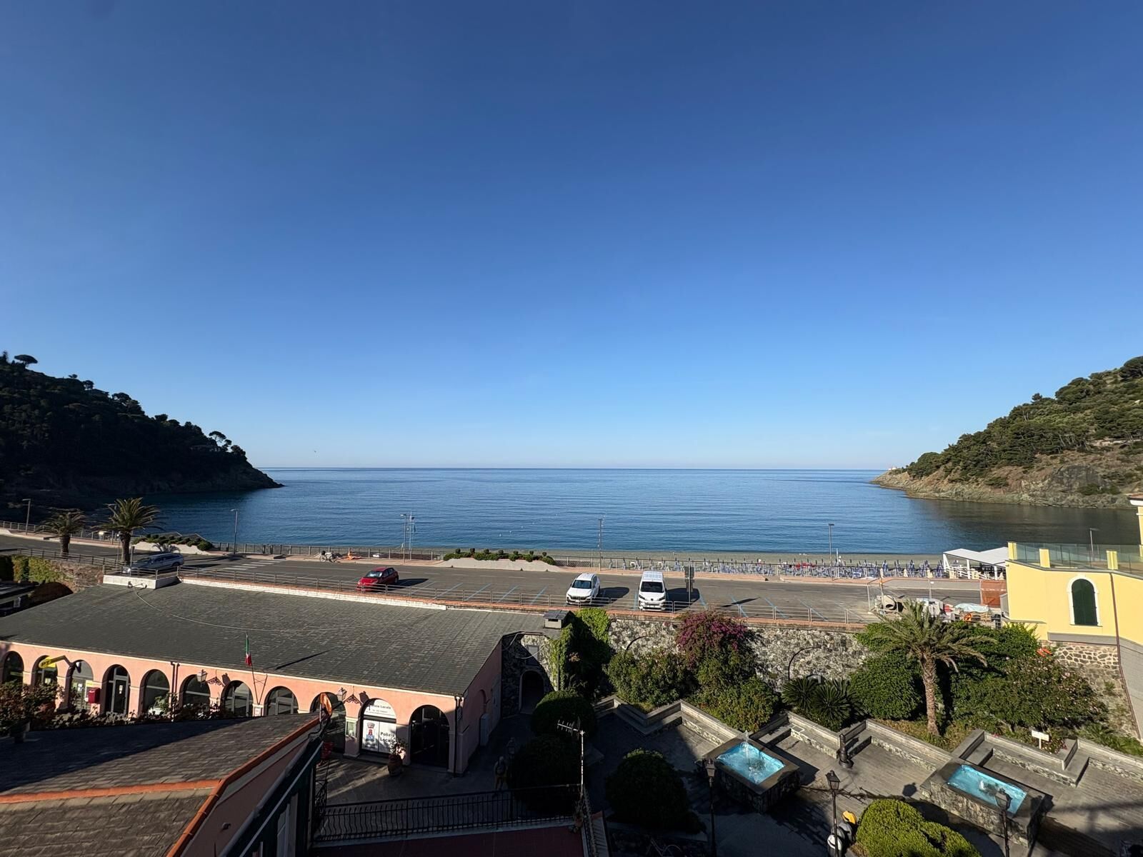A coastal view with a clear sky, a parking area, and a building with arches.