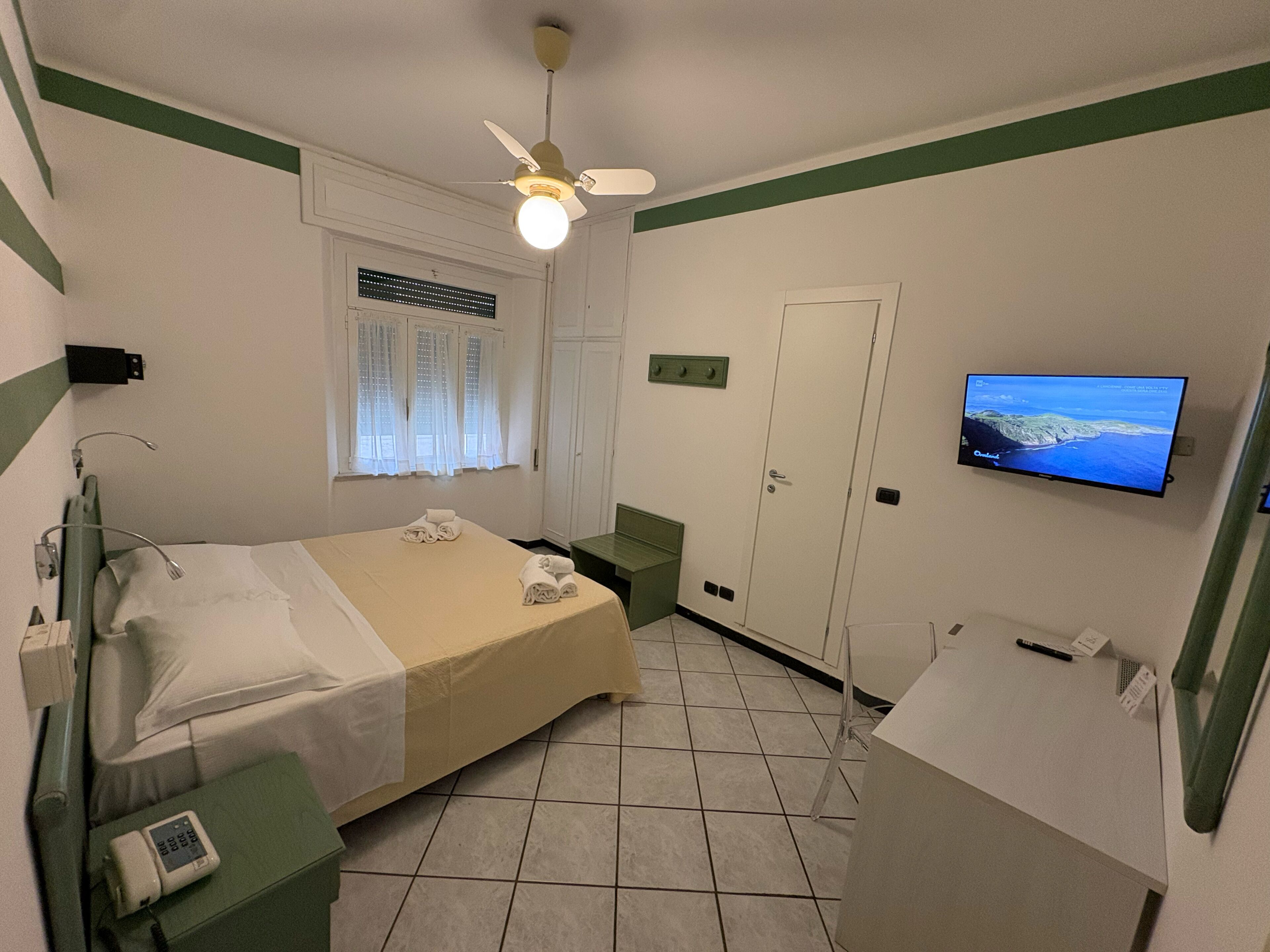 A hotel room with a bed, a television, a desk with a telephone, and a window with curtains.