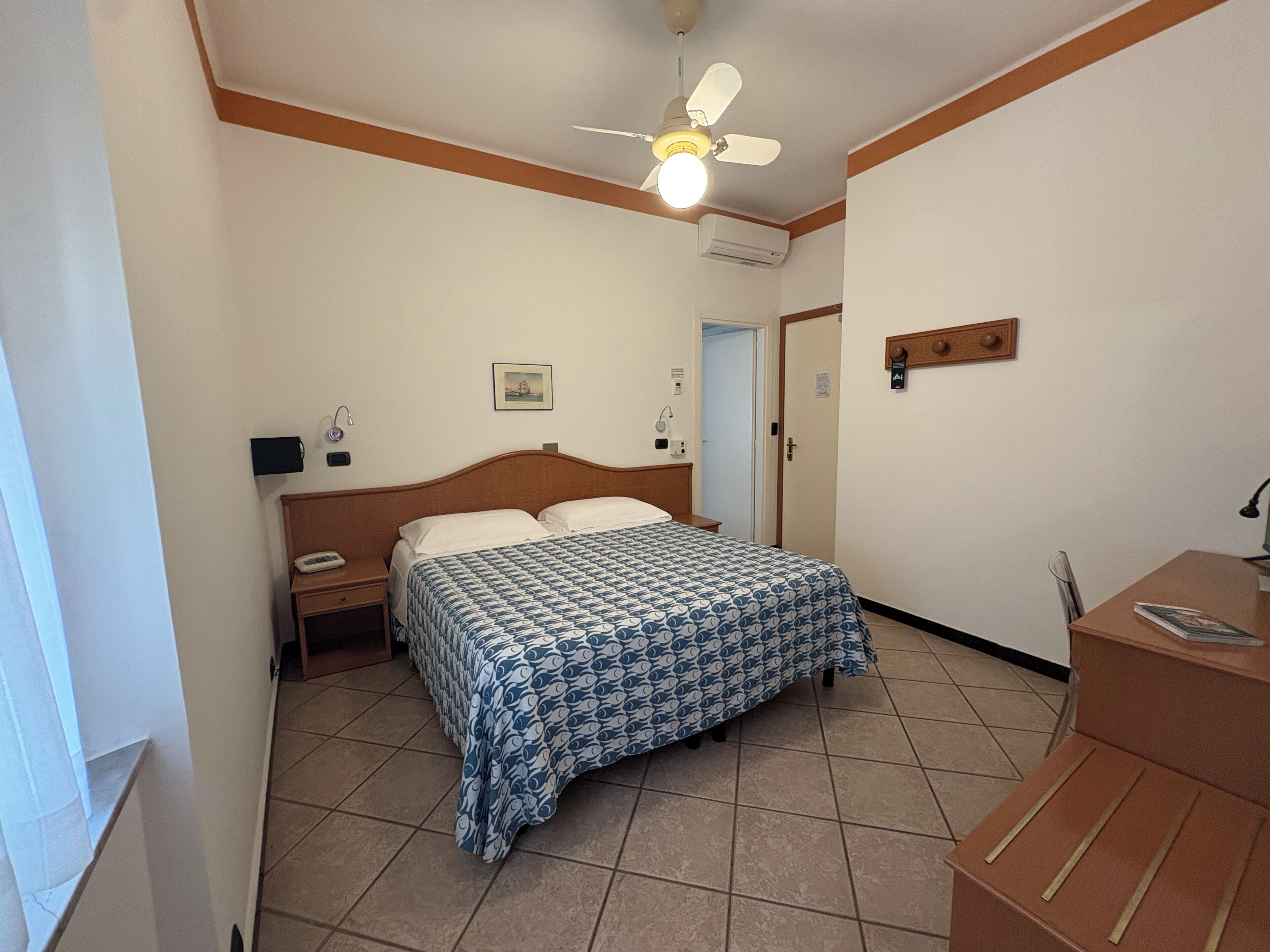 A bedroom with a bed, bedside table, nightstand, ceiling fan, air conditioning unit, and a door.