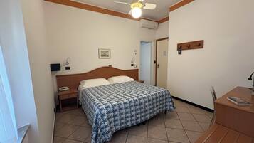 A bedroom with a bed, bedside table, nightstand, ceiling fan, air conditioning unit, and a door.