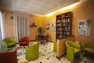 Una biblioteca con sillas verdes, una mesa y una estantería.
