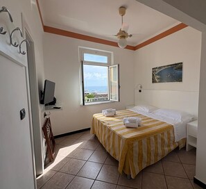 A hotel room with a bed, a TV, a window with a view, and a ceiling fan. - Hotel delle Rose (Bonassola)