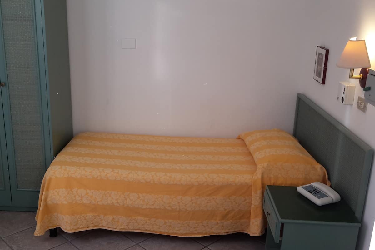 A single bed with a floral-patterned bedspread, a bedside table with a lamp, and a phone.