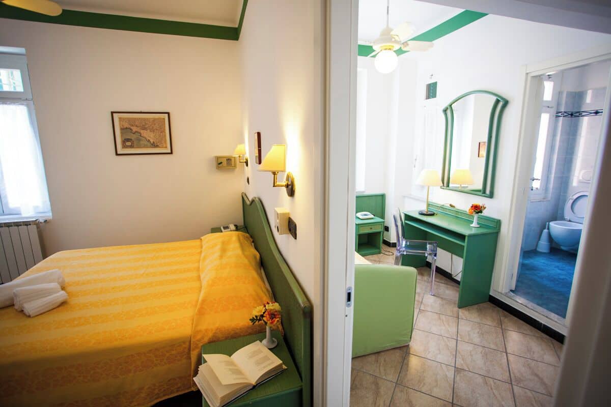 A hotel room with a bed, bedside table, lamp, mirror, and a view of the bathroom.
