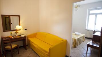 Une pièce avec un canapé jaune, un bureau avec une lampe, une chaise et un lit recouvert d’une couverture à rayures.