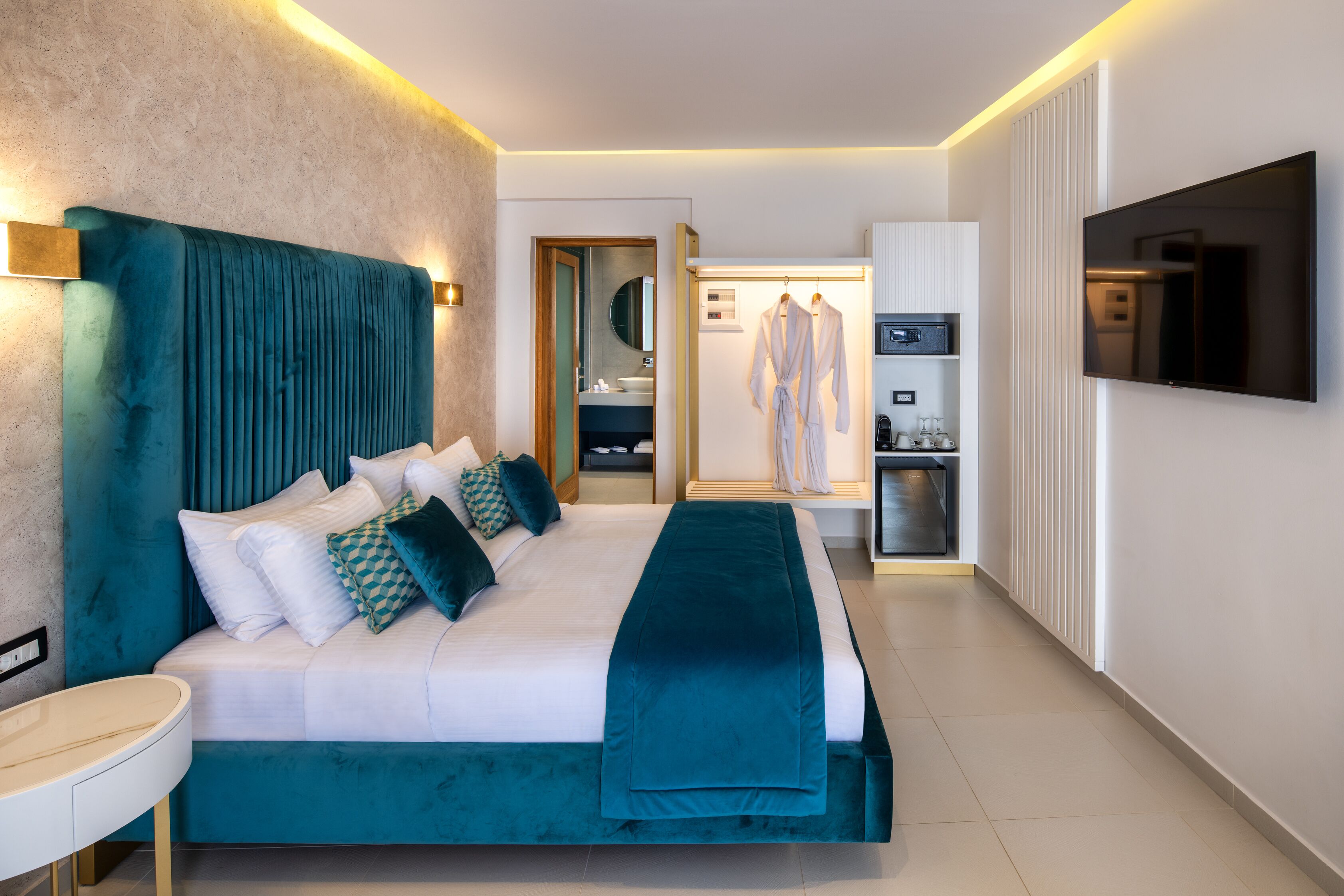 Una habitación de hotel moderna con una cama grande, una mesita de noche, un televisor y un baño visible a través de una puerta abierta.