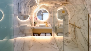 Une salle de bain luxueuse avec un sol en marbre, un lavabo central et une douche séparée par des parois en verre.