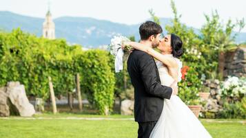 Un couple s’embrasse dans un jardin, avec un mur de pierre et de la verdure en arrière-plan.