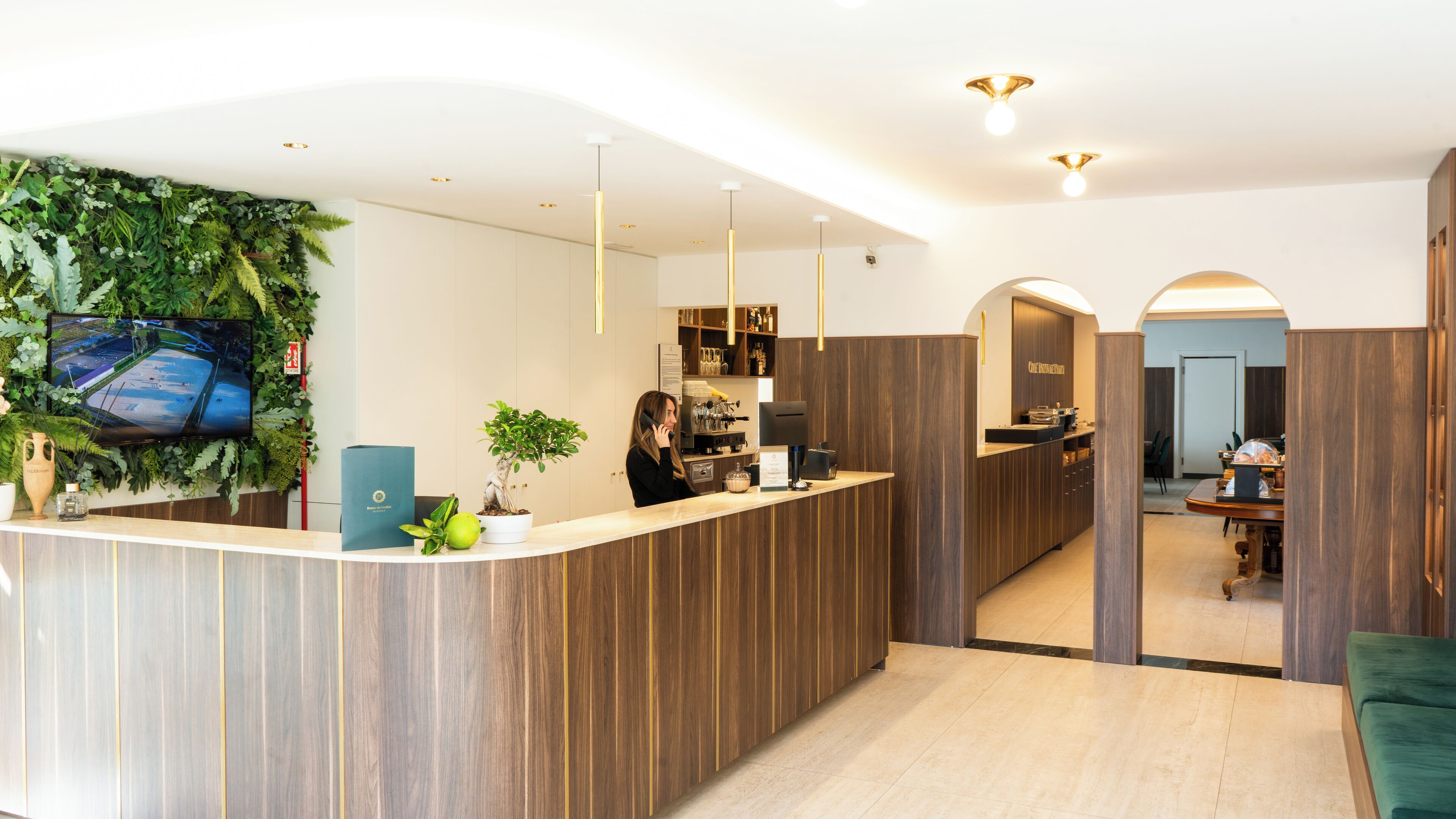 A reception area with a wooden reception desk, a potted plant, a coffee machine, and a television mounted on the wall.