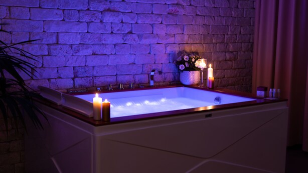 A rectangular bathtub with two lit candles, a flower arrangement, and a bottle of lotion on the edge. - Resort & Winery Bosco De Medici  (Pompei)