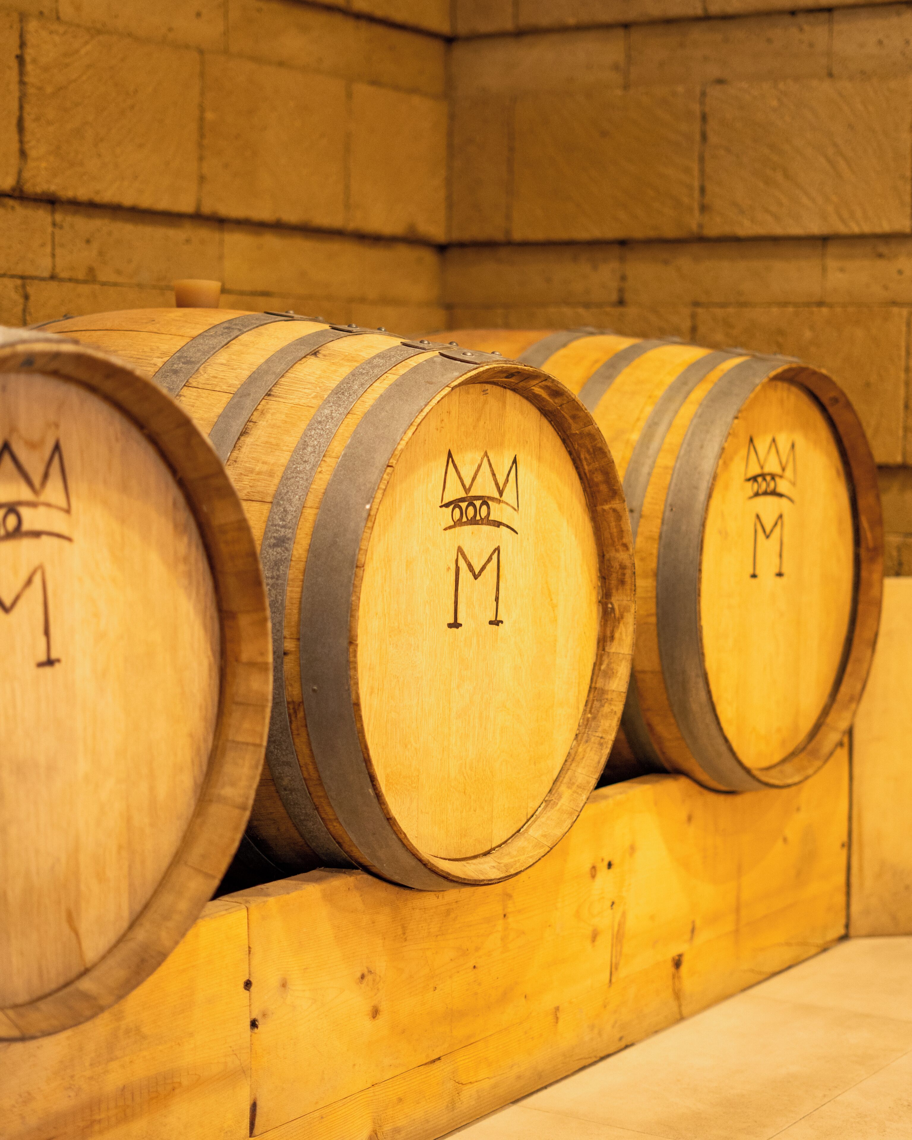 Wooden barrels with crown symbols, arranged in a row against a stone wall.