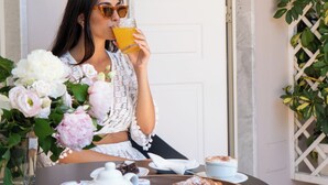 A woman sitting at a table with a floral arrangement, a teapot, a cup of coffee, and a pastry. - Resort & Winery Bosco De Medici  (Pompei)