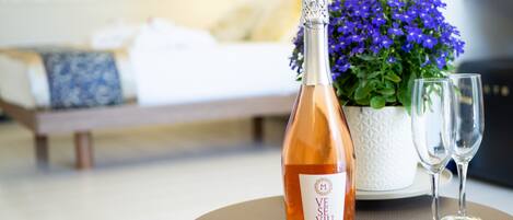Une bouteille de vin Veuve, deux verres à vin et une plante en pot aux fleurs violettes, le tout posé sur une table dans une chambre d’hôtel.