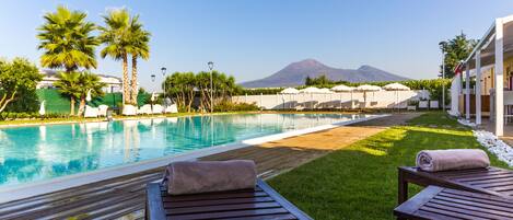A poolside area with lounge chairs, a wooden table, and umbrellas.