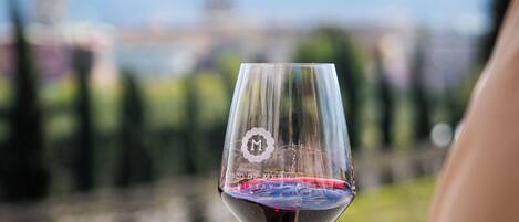 A wine glass with a reflection, held by a person, with a blurred cityscape and mountains in the background.