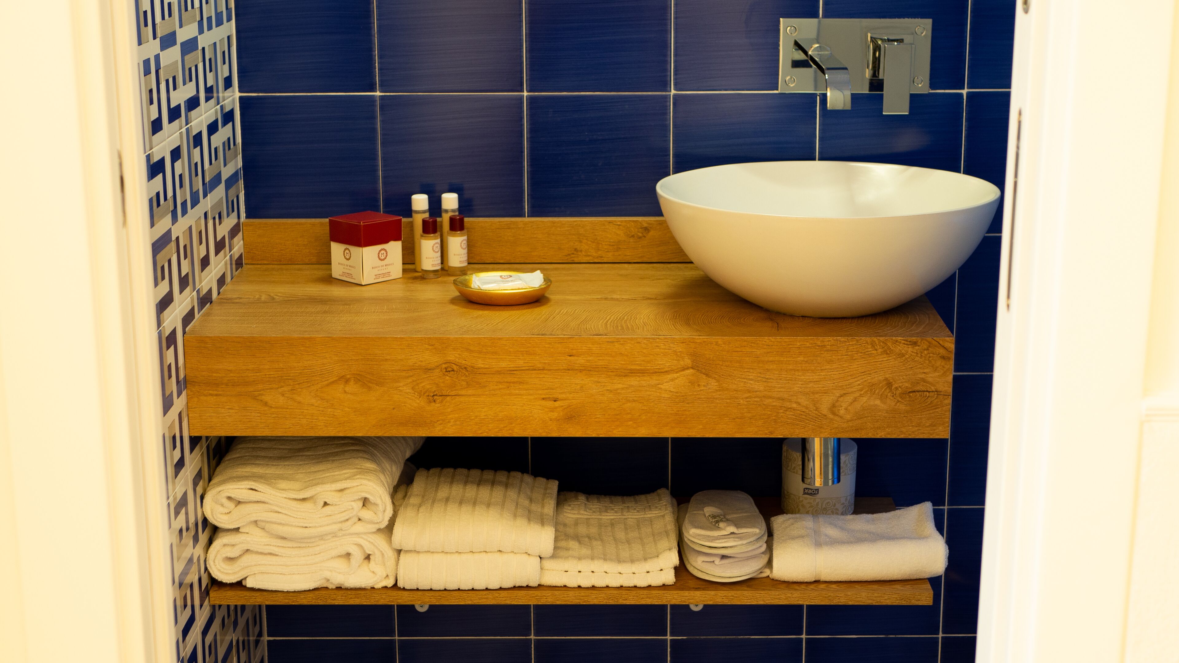 A bathroom with a wooden vanity, a white sink, and blue tiles.