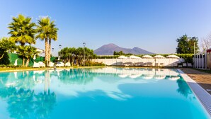 A swimming pool with clear blue water, surrounded by palm trees and lounge chairs. - Resort & Winery Bosco De Medici  (Pompei)