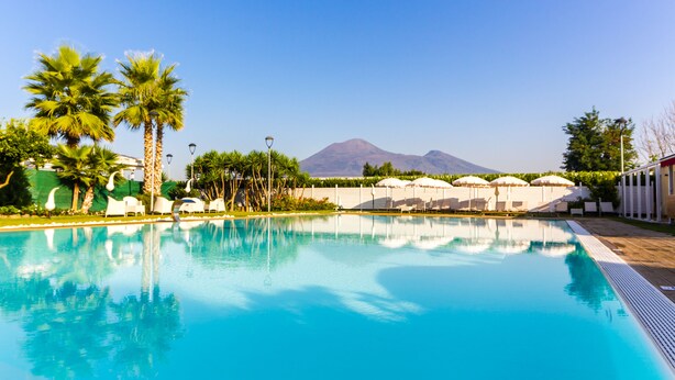 A swimming pool with clear blue water, surrounded by palm trees and lounge chairs. - Resort & Winery Bosco De Medici  (Pompei)
