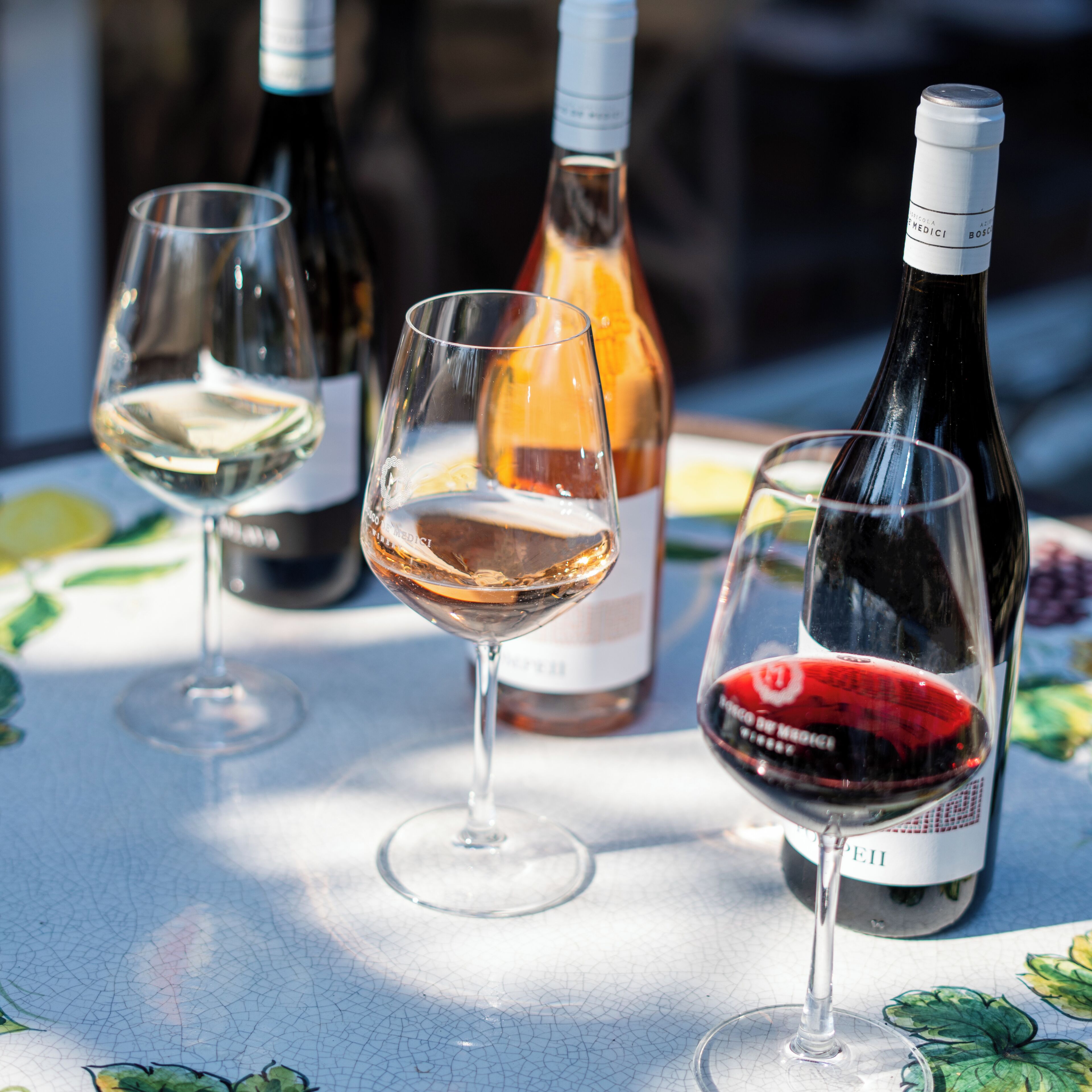 A table with wine glasses and bottles, a patterned tablecloth, and a clear view of the sky.