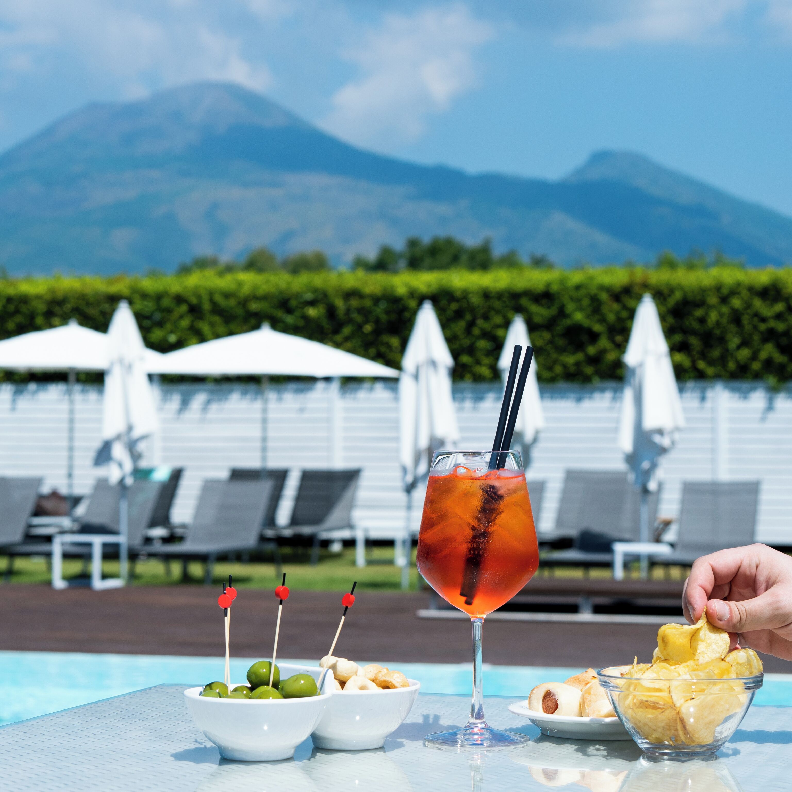 Un espace aménagé au bord de la piscine, avec des chaises longues, une table où sont servis des plats et des boissons, et une vue sur les montagnes en arrière-plan.