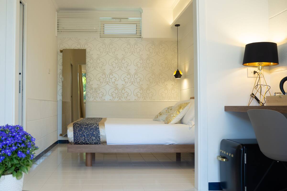 Ein modernes Schlafzimmer mit Bett, Nachttisch, Lampe und einer Zimmerpflanze.