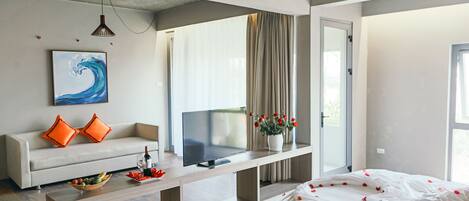 Una habitación de hotel moderna con sofá, televisor de pantalla plana, mesa de comedor y cama con pétalos de rosa.
