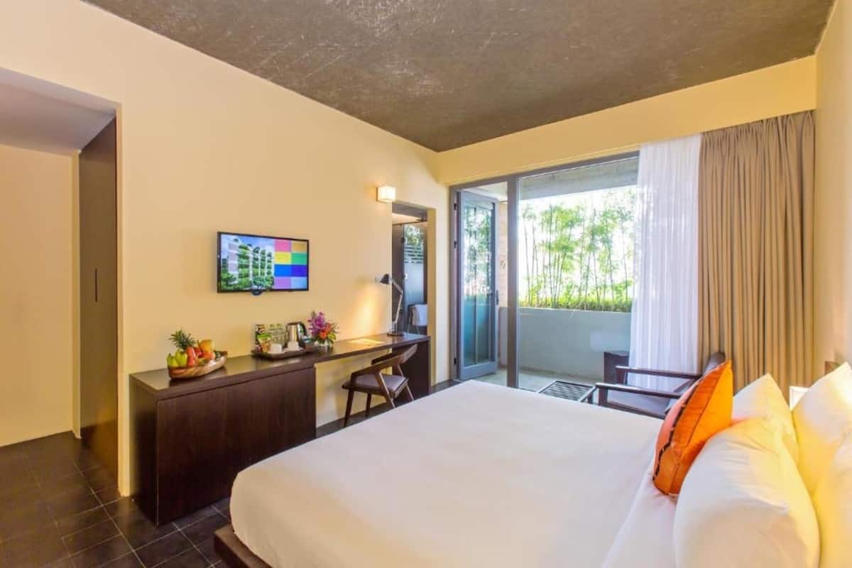 A hotel room with a bed, a desk, a TV, and a balcony with a view.