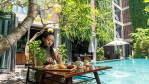 Mesa de comedor con comida y bebidas, una piscina y follaje en un edificio moderno.