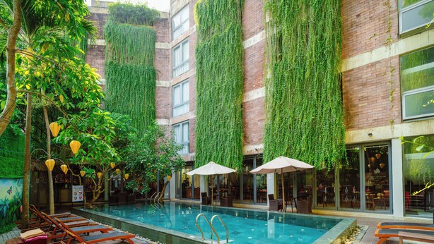 Piscina en la azotea con sillones y sombrillas, rodeada de vegetación y muros de ladrillo.