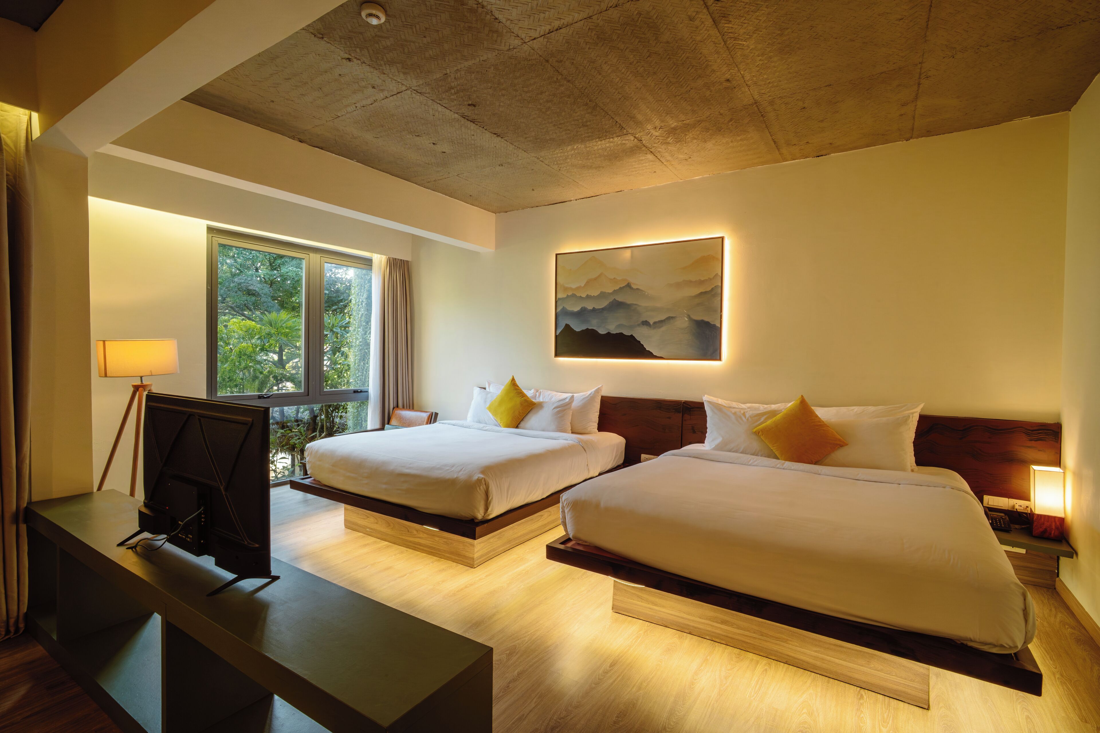 A hotel room with two beds, a desk, a TV, and a painting on the wall.