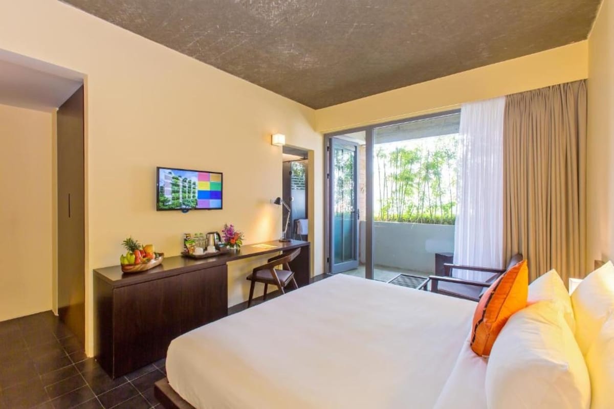 A hotel room with a bed, a desk, a TV, and a balcony with a view.