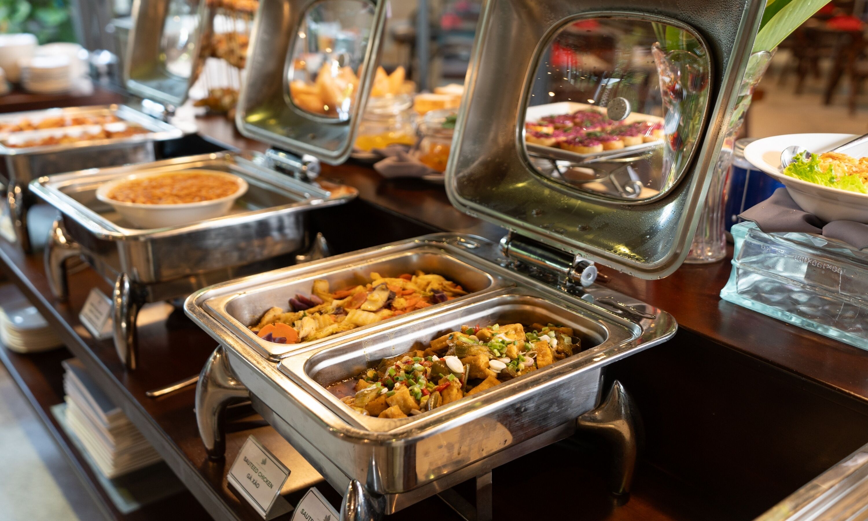 Ein Buffet mit verschiedenen Speisen, darunter gekennzeichnete Gerichte wie 'SAUTEED CHICKEN' und 'SAUTEED VEGETABLES'.